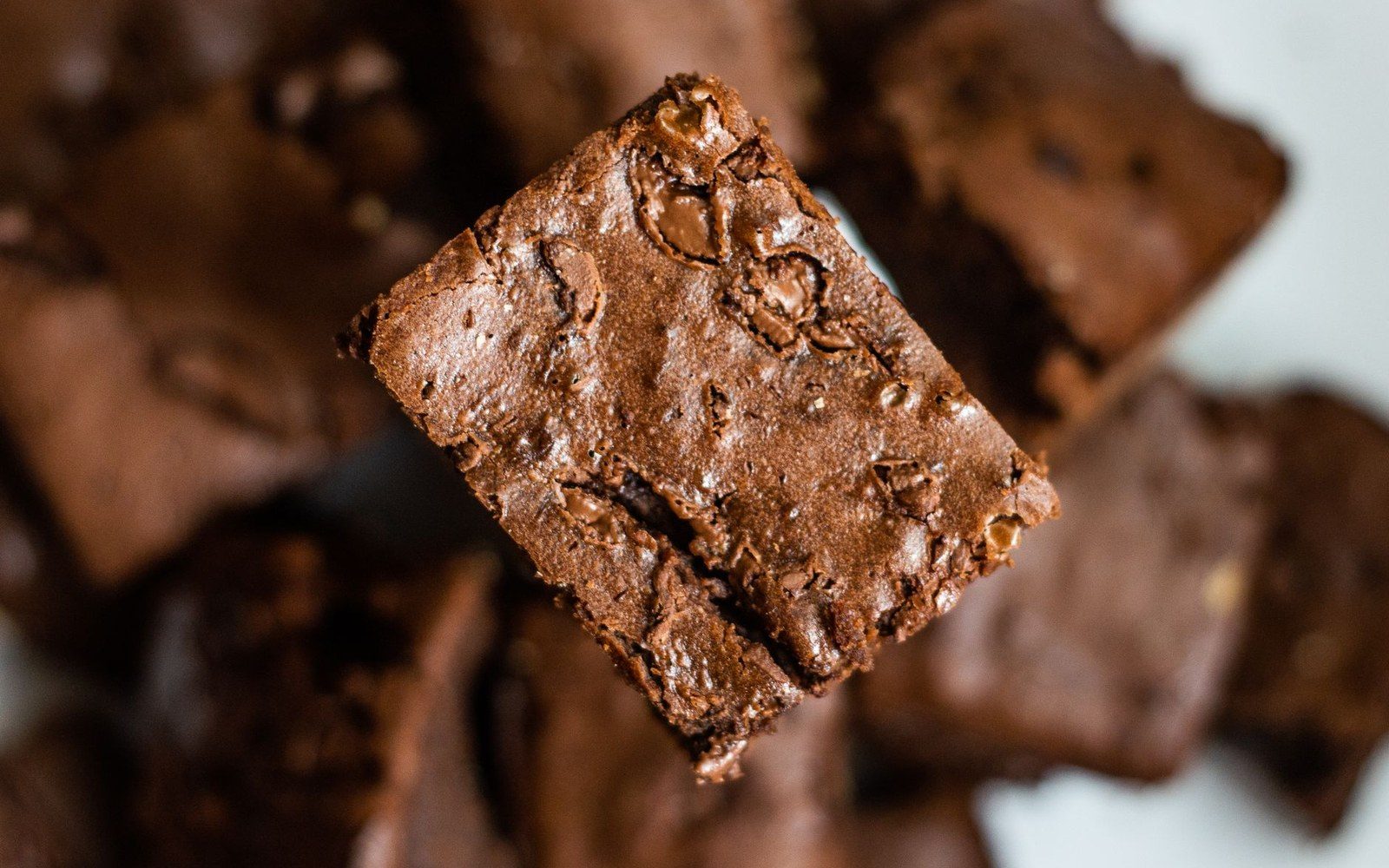 A brownie tray cut into squares, one piece lifted to show the dense fudgy crumb and the thin crust on the edge