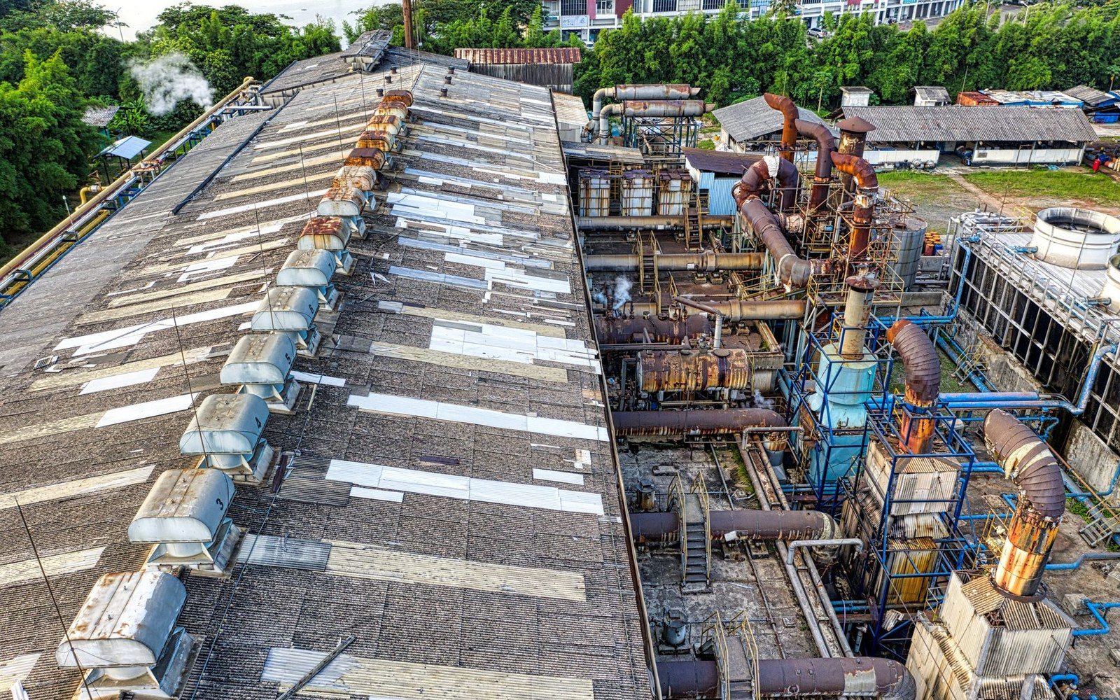 An aerial view of a long industrial processing plant — ranked roof vents, pipework and cooling towers