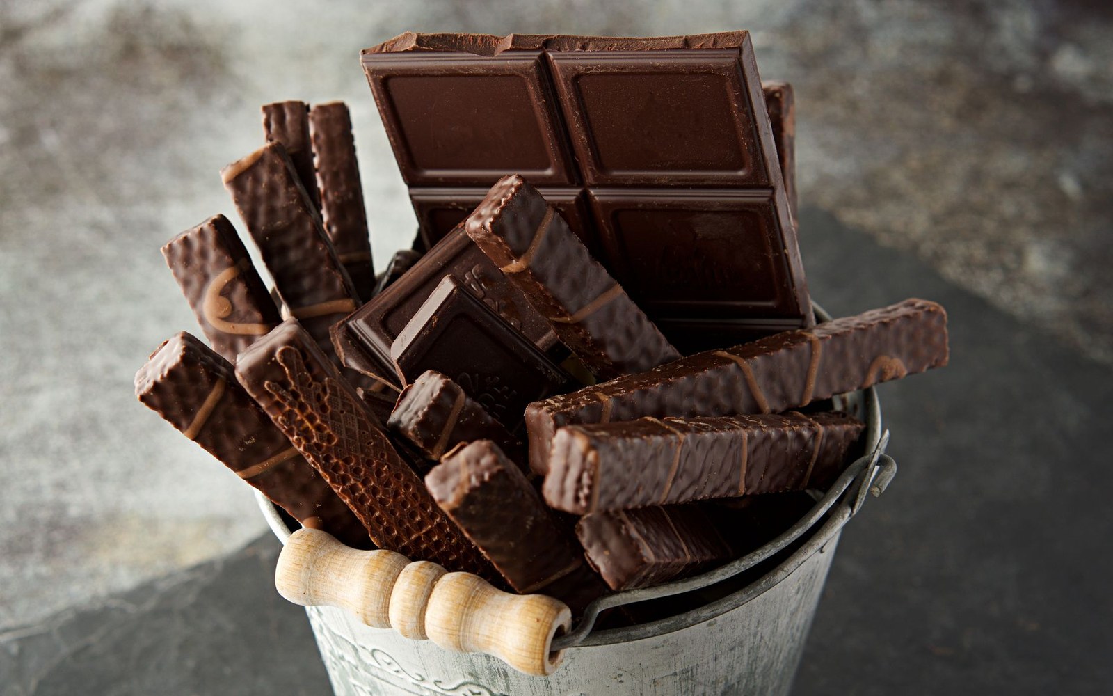 A metal bucket packed upright with dark chocolate bars and chocolate-coated wafer sticks