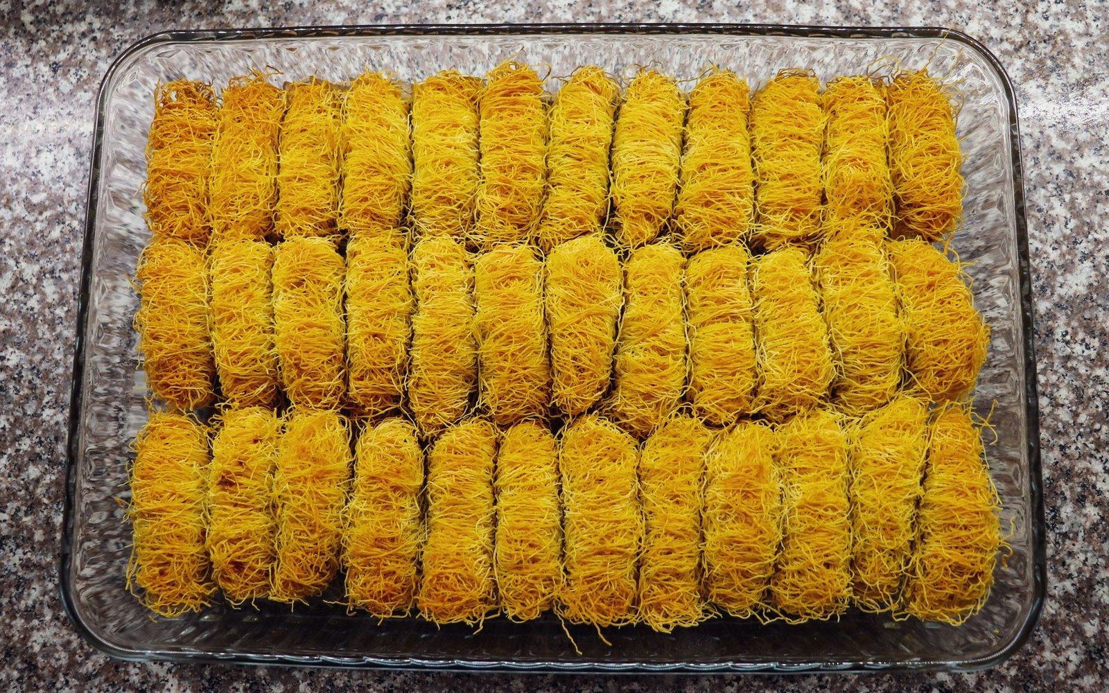 A glass tray holding neat rows of golden shredded kataifi pastry