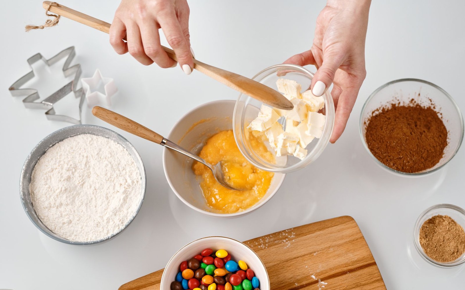 An overhead baking bench: hands mixing in a bowl, with flour, cocoa, beaten egg, butter and chocolate buttons alongside