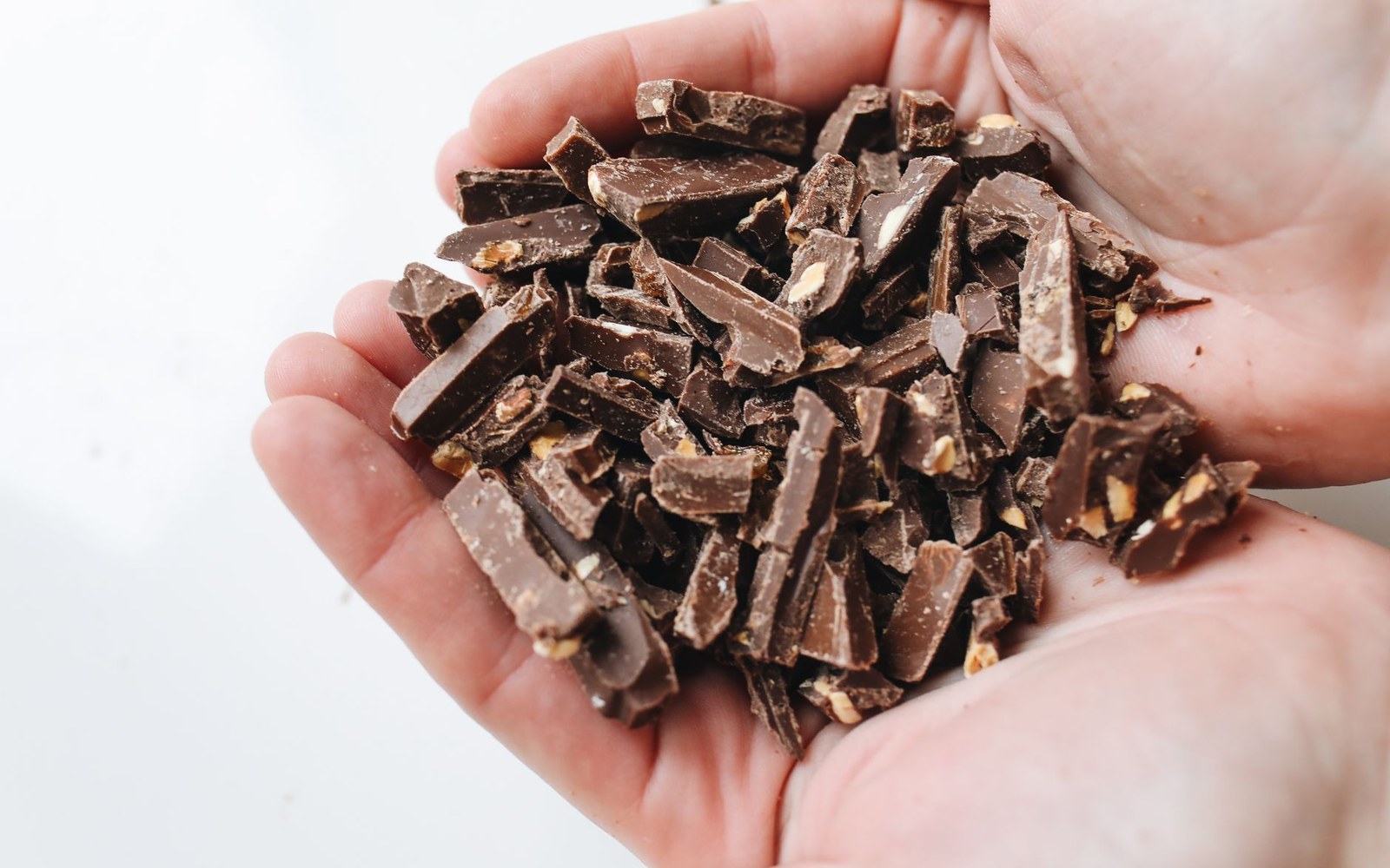 Two cupped hands holding roughly chopped dark chocolate