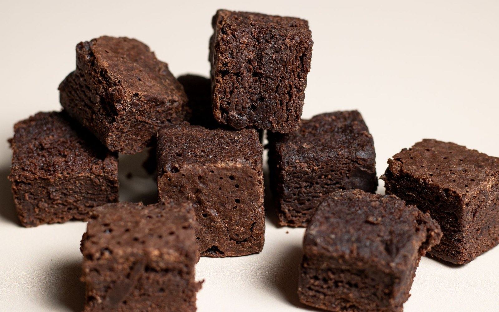 A stack of dense, dark brownie cubes on a pale ground