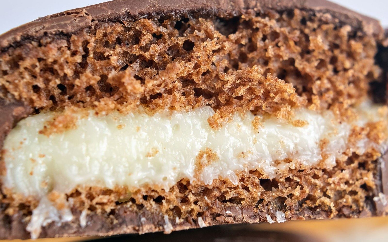 An extreme close-up cross-section of a chocolate-coated cake showing an open crumb and a pale cream layer