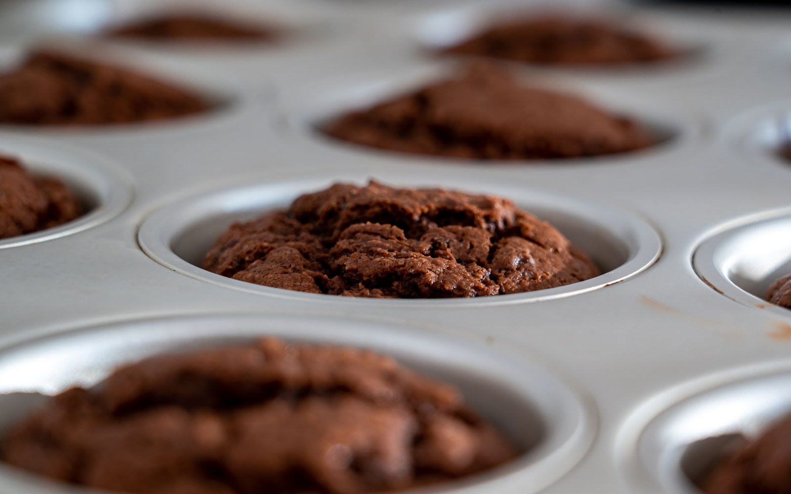 Chocolate cakes risen in the wells of a metal muffin tin