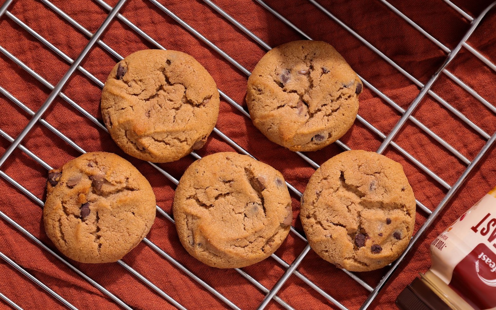 Chocolate-chip cookies cooling on a wire rack over a rust-coloured cloth
