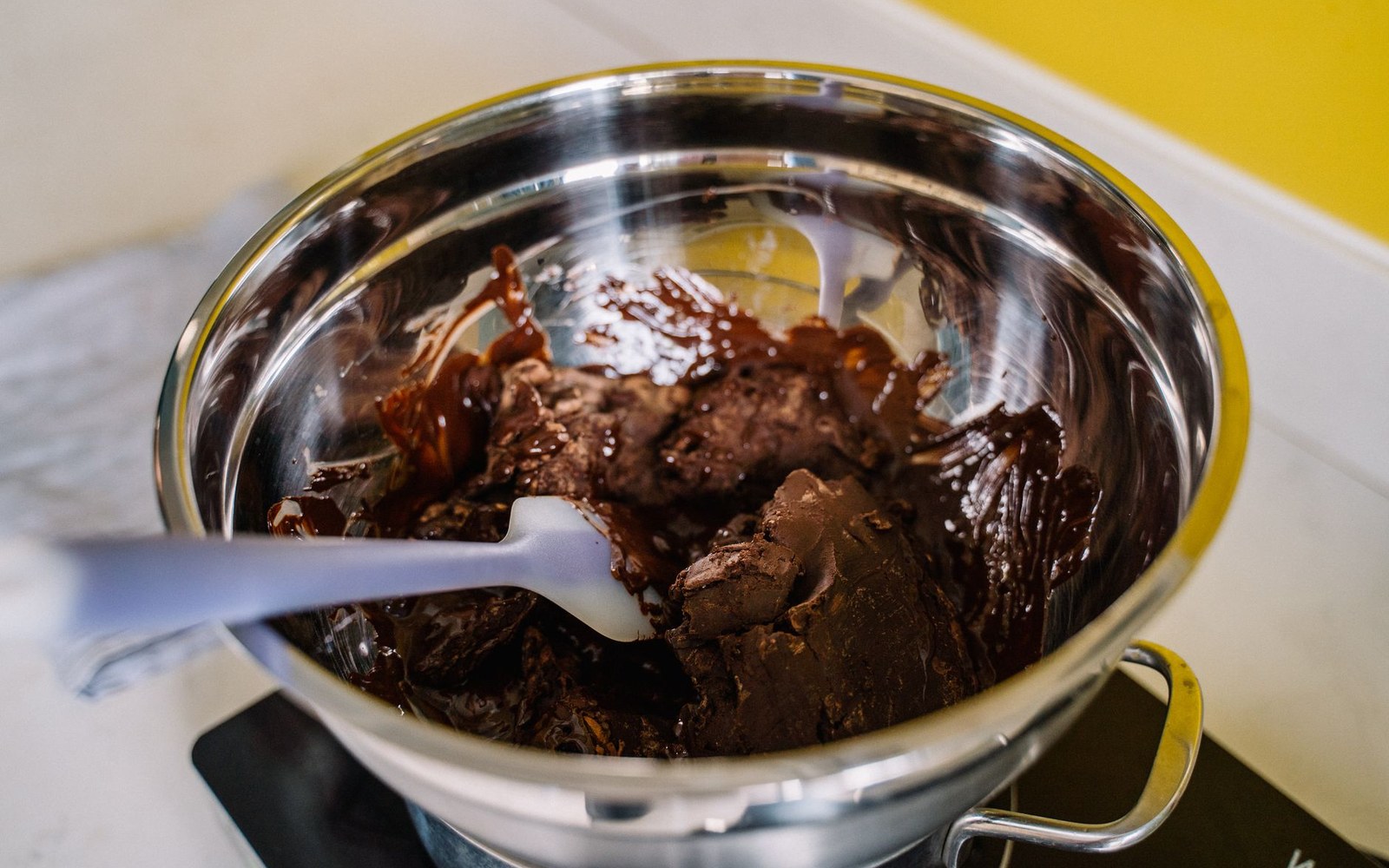 A metal bowl of thick, dull melted chocolate being worked with a spatula